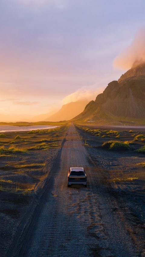 Gravel road at a golden Sunset with Vestrahorn mountain in the background and a car driving the road in Iceland